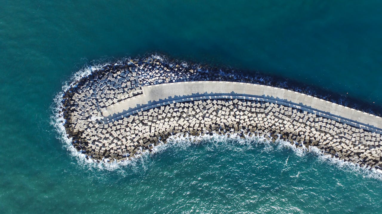 An aerial view of coastal breakwater structures in Ashdod, Israel, with waves crashing against them.
